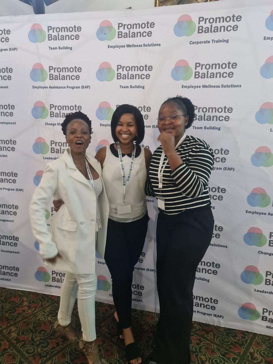 Three delegates smiling in front of the Promote Balance backdrop